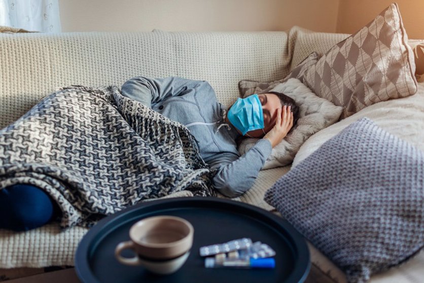 Sick woman having flu or cold. Girl lying in bed having headache wearing protective mask by pills and water on table. (Sick woman having flu or cold. Girl lying in bed having headache wearing protective mask by pills and water on table., ASCII, 118 co